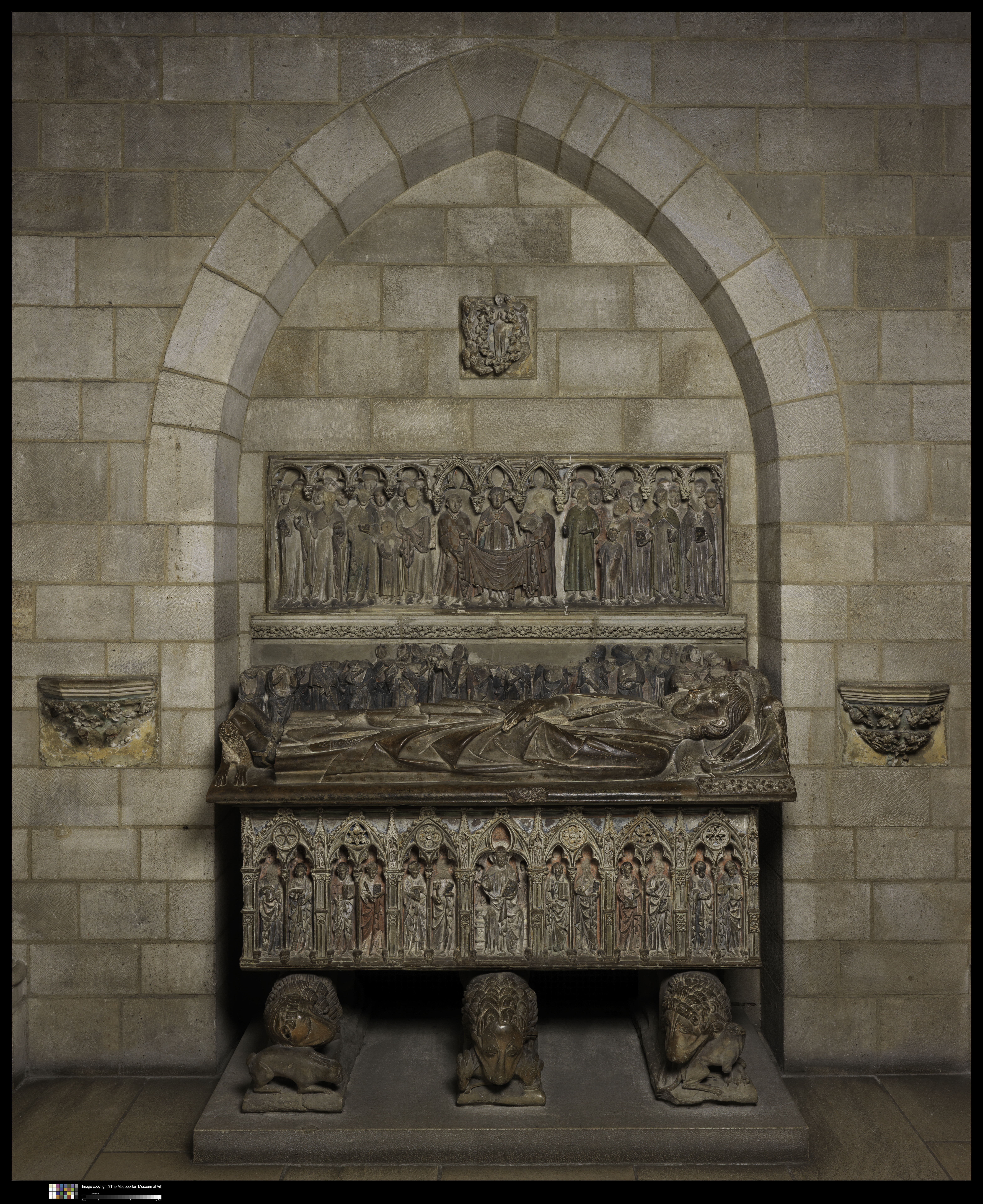 Tomb sculpture of a recumbent man holding a sword celebrated by rows of mourners behind him, over a sarcophagus with figures of Christ and apostles. The ensemble is carved in limestone with polychromy.
