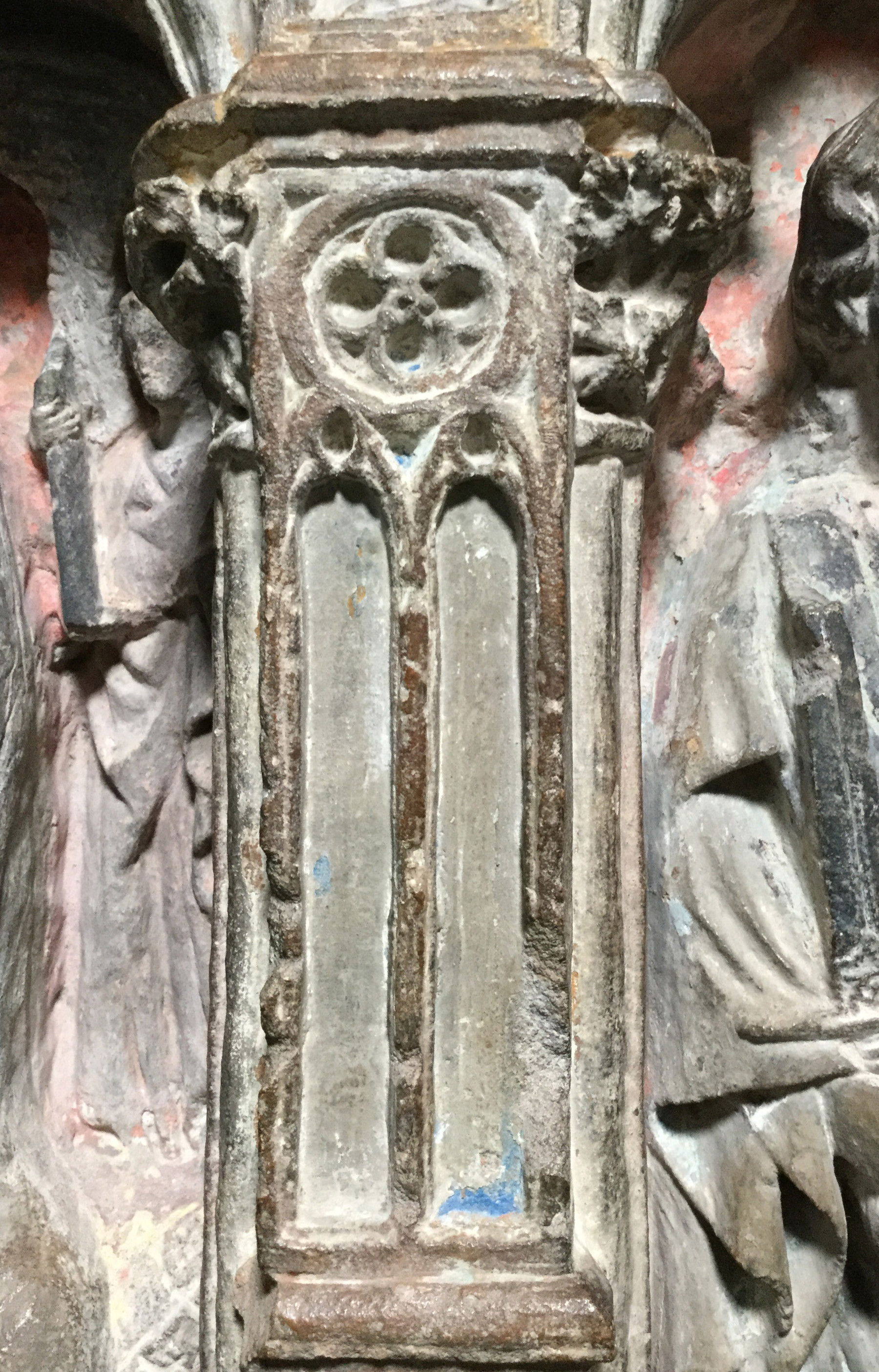 Carved miniature stone window in gothic style, covered by a thick modern layer of grey lime, except for a small area of azurite blue appearing under the overpaint on the bottom right.