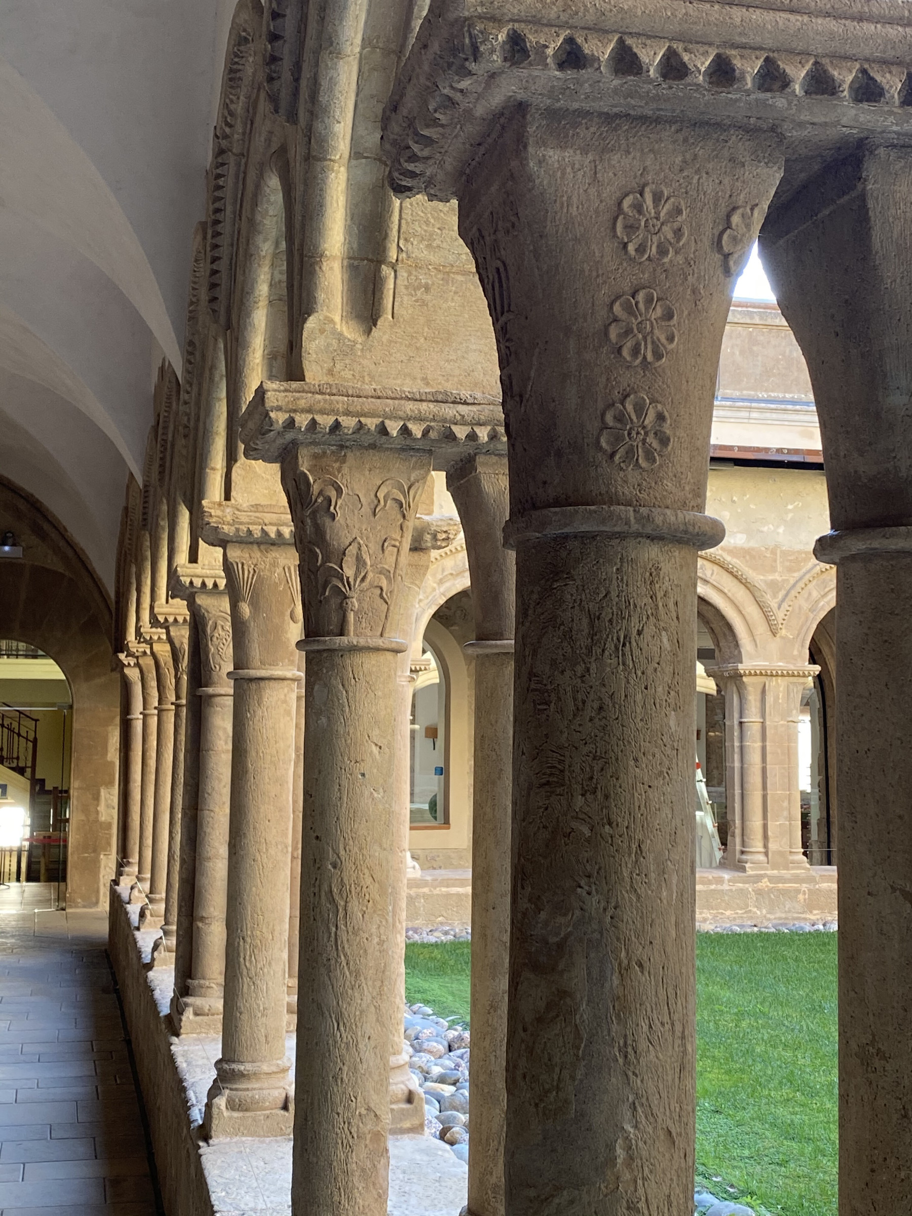 Cloister with stone arches supported by double columns and capitals decorated with bas-relief flowers or foliage, with carved tooth friezes on abaci.