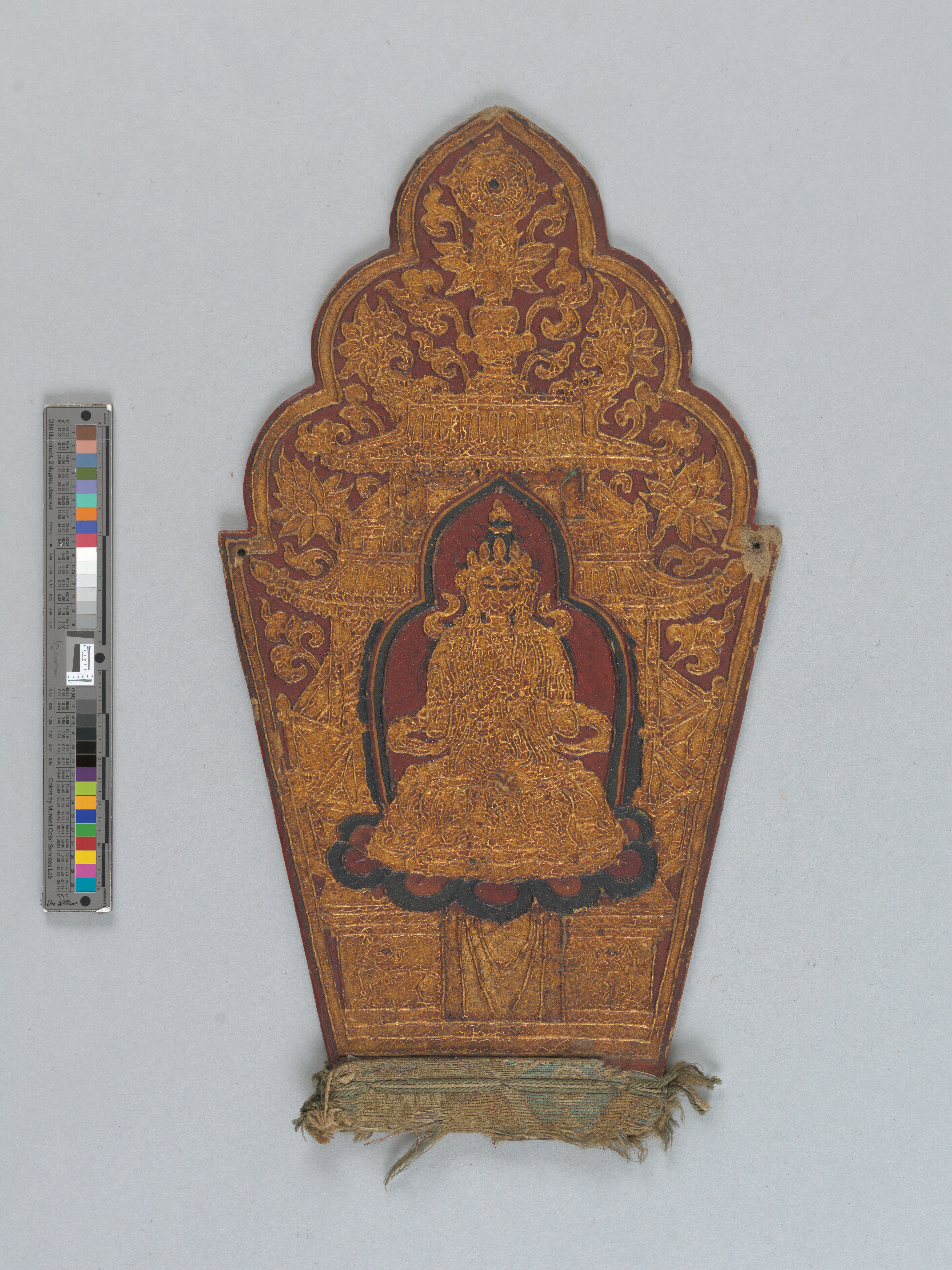 Torana-shaped panel with gilded raised decoration depicting a seated figure with some outlines in black and a red background.